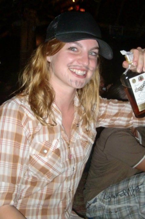 A woman in a plaid shirt is holding a bottle of jack daniels