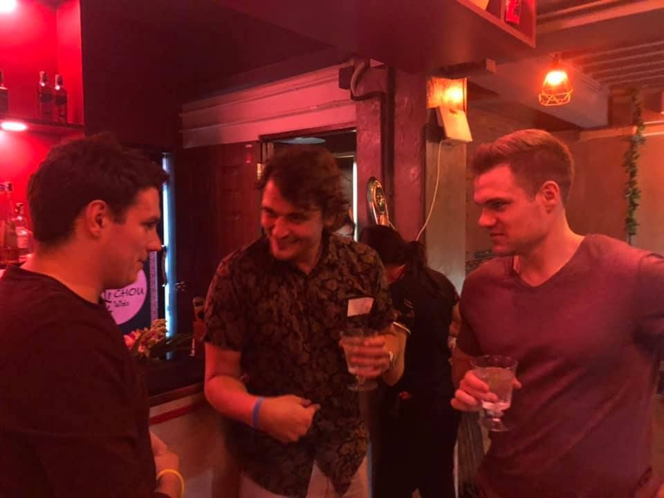 Three men are standing next to each other in a dark room holding drinks.