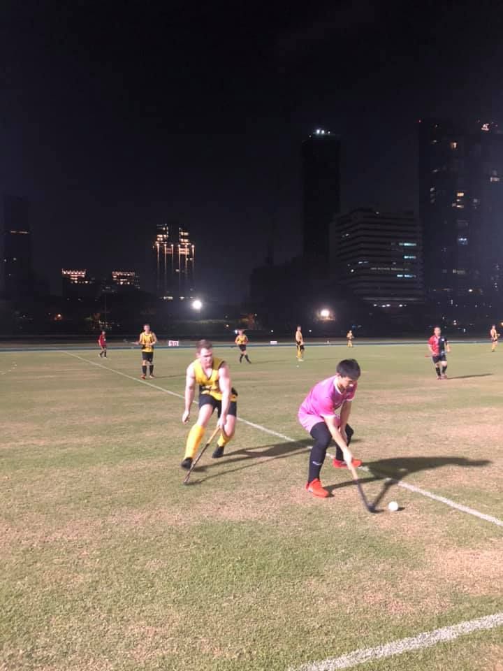 A group of people are playing field hockey on a field at night.