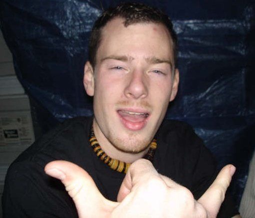 A young man wearing a black shirt and a necklace is making a funny face.