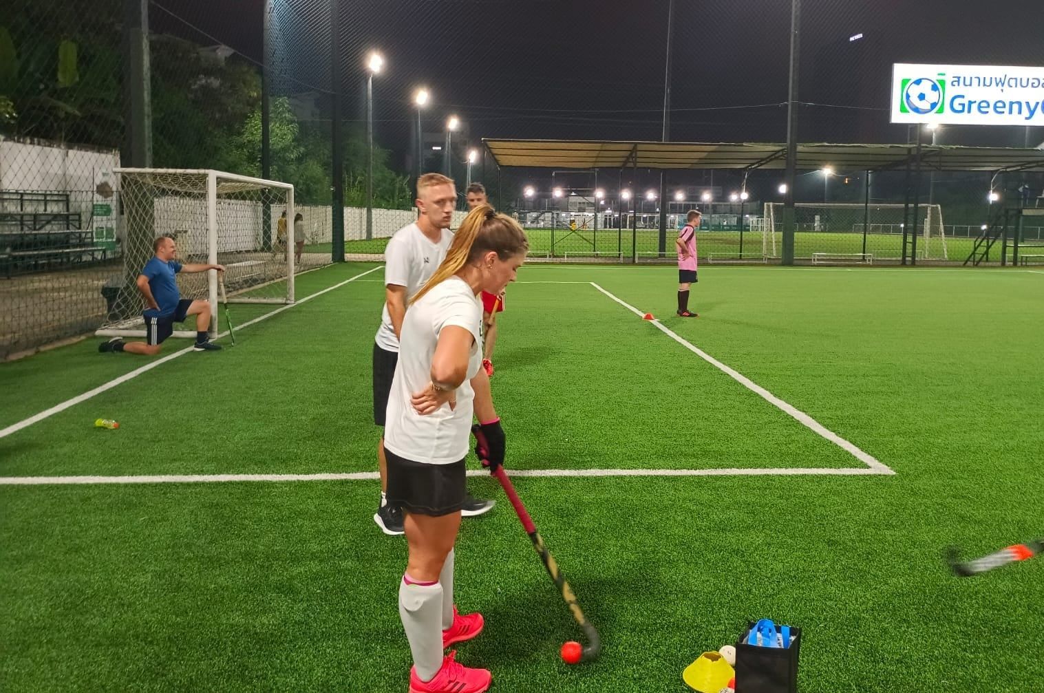 A group of people are playing field hockey on a field at night.