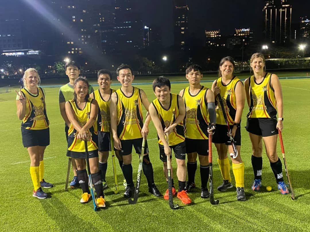 A group of field hockey players are posing for a picture on a field at night.