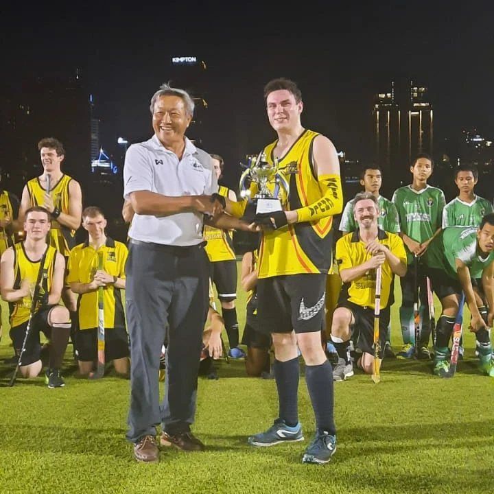 A man is holding a trophy in front of a field hockey team