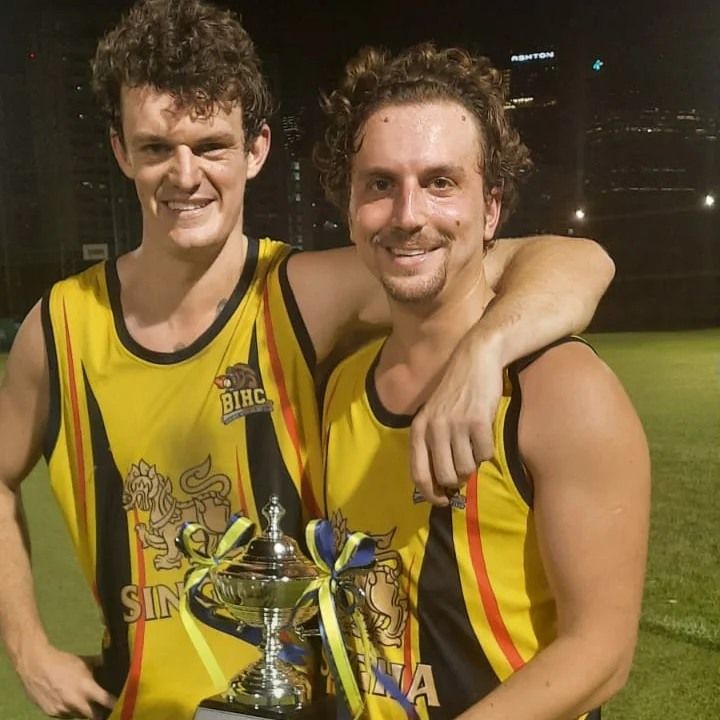 Two men in yellow tank tops holding a trophy with the word sin on it