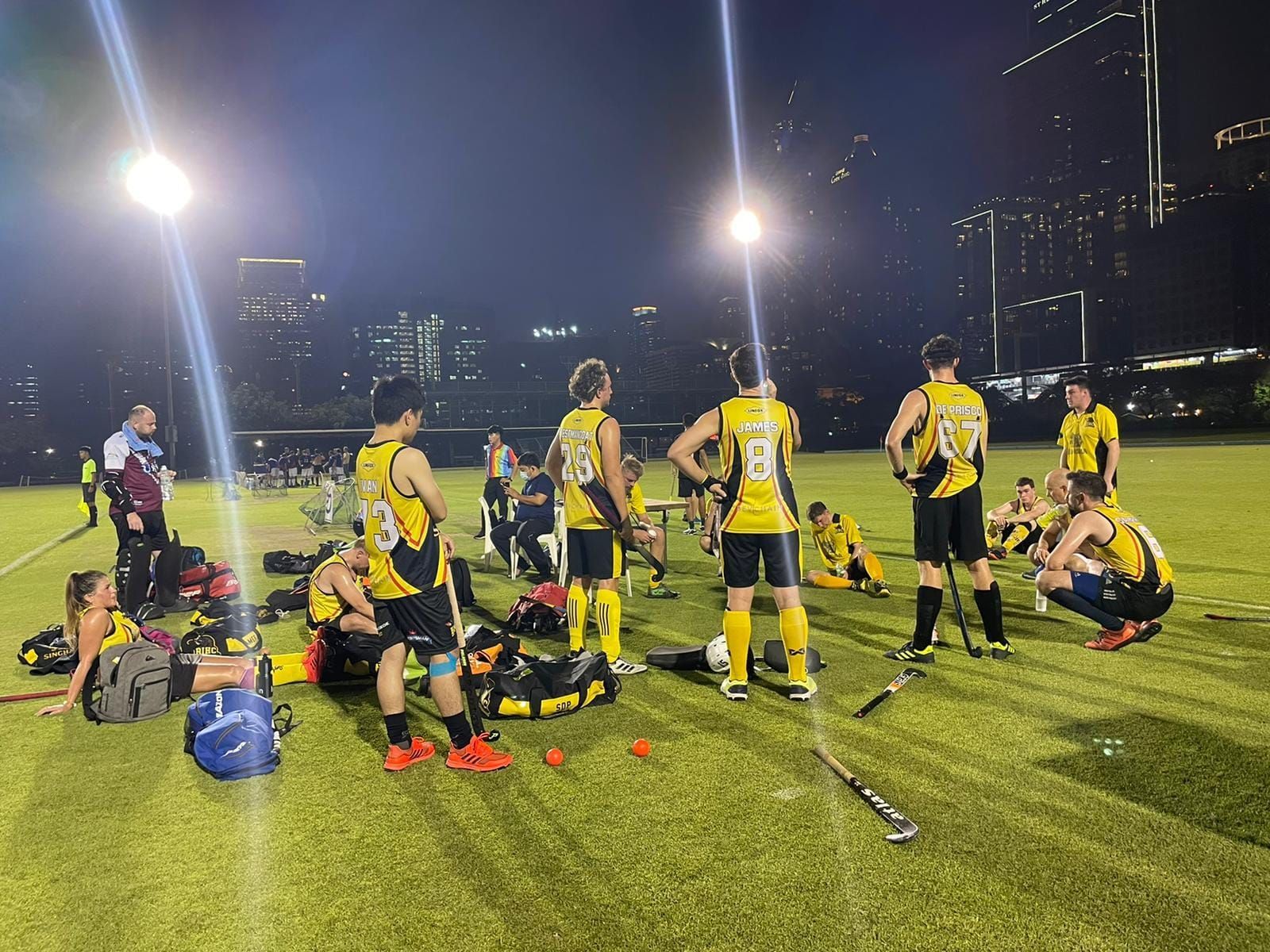 A group of people are standing and sitting on a field at night.
