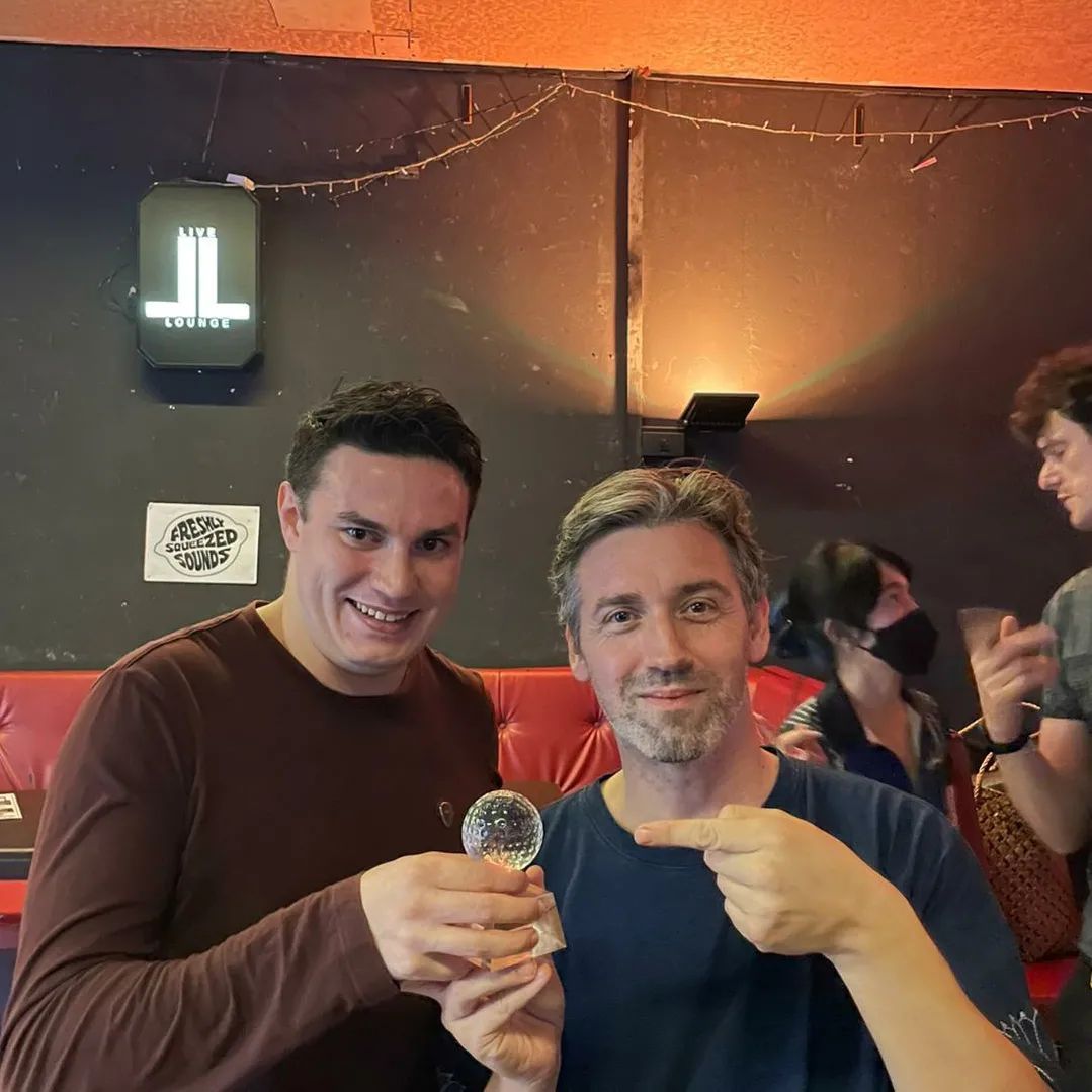 Two men are posing for a picture in front of a sign that says jl