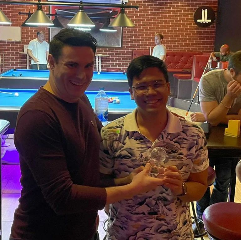 Two men are posing for a picture in a pool hall.