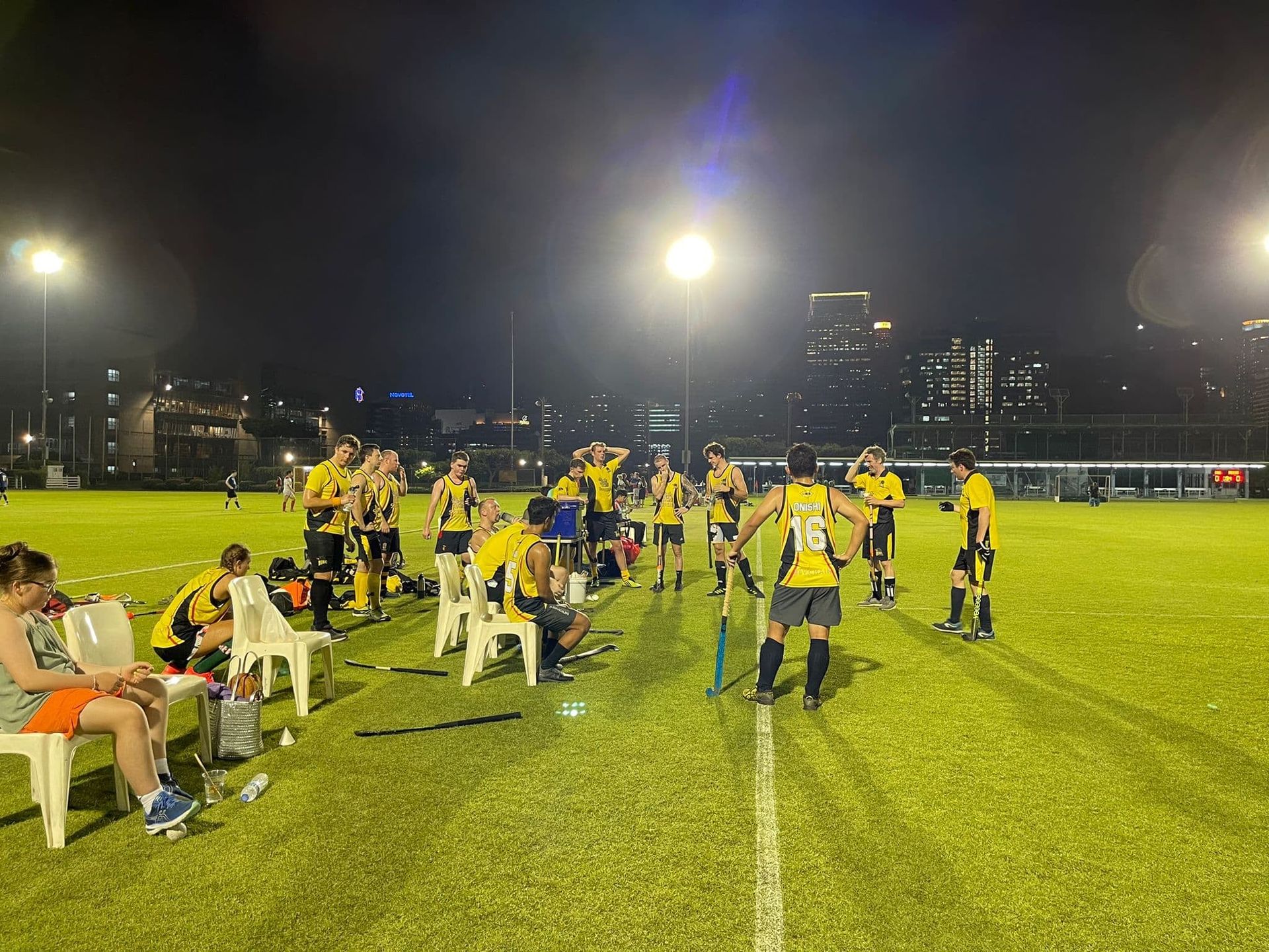A group of people are playing field hockey on a field at night.