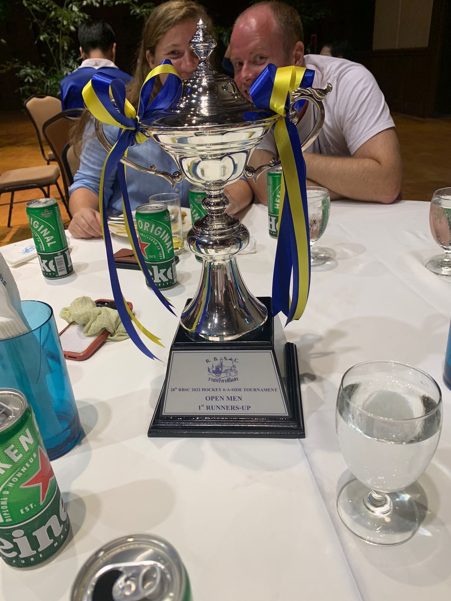 A man and woman are sitting at a table with a trophy on it.