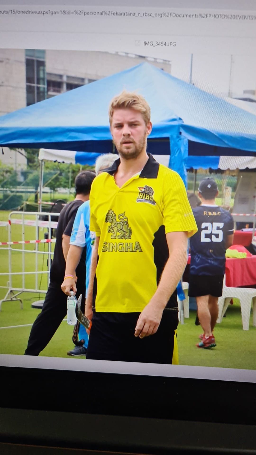 A man in a yellow shirt is standing in front of a blue tent.