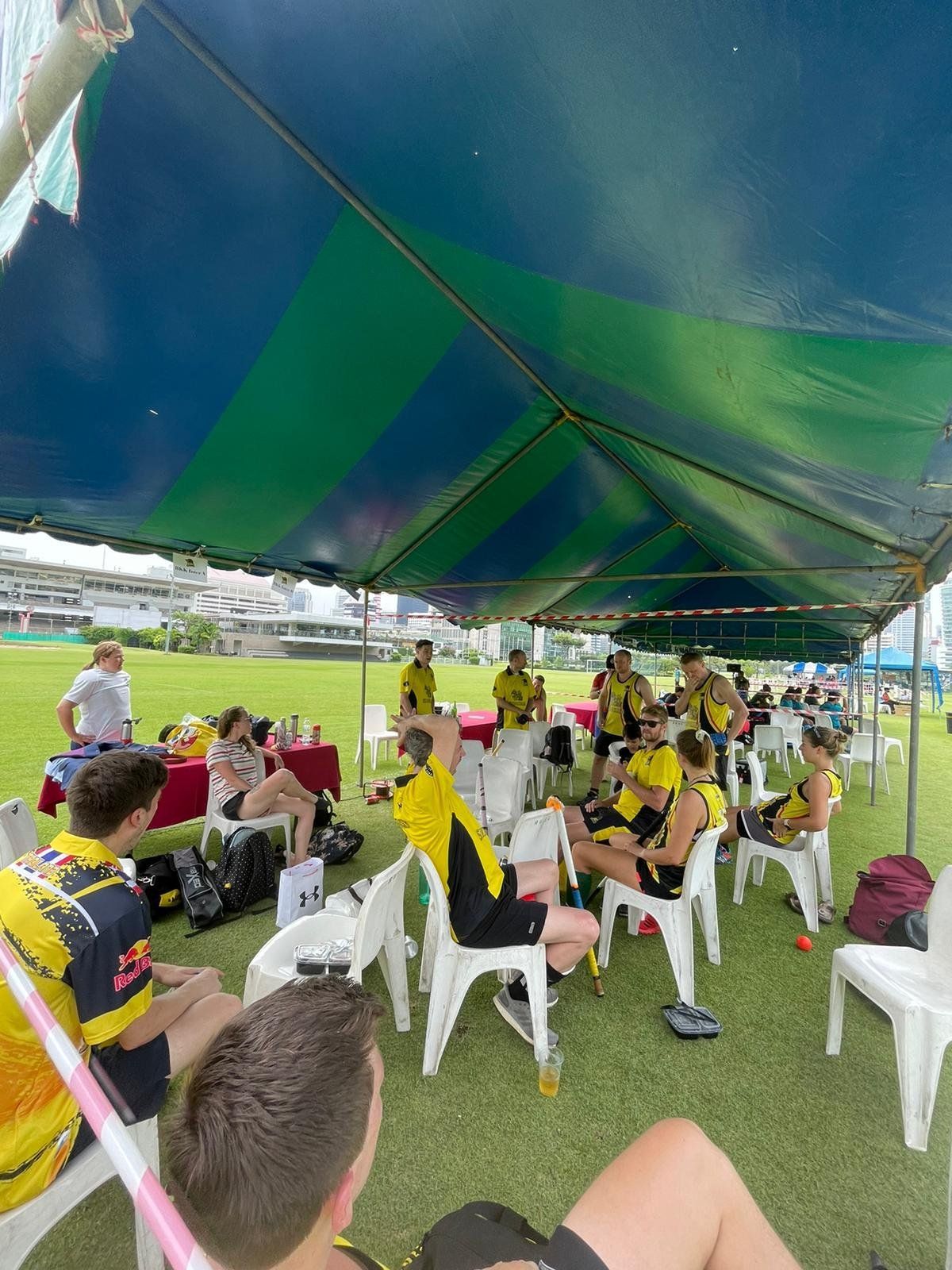 A group of people are sitting under a tent in a field.