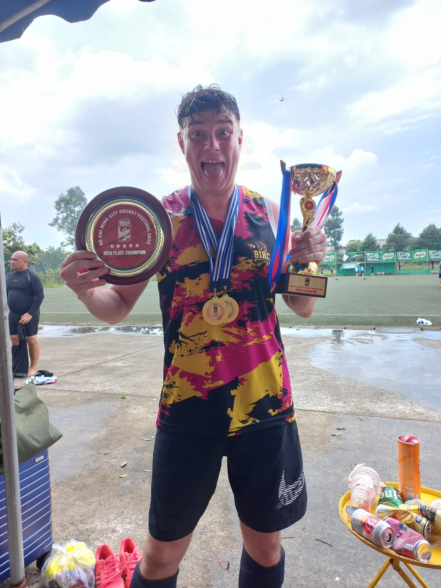 A man is holding two trophies and a medal around his neck.