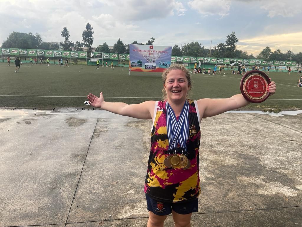 A woman is holding a frisbee and a medal in front of a soccer field.