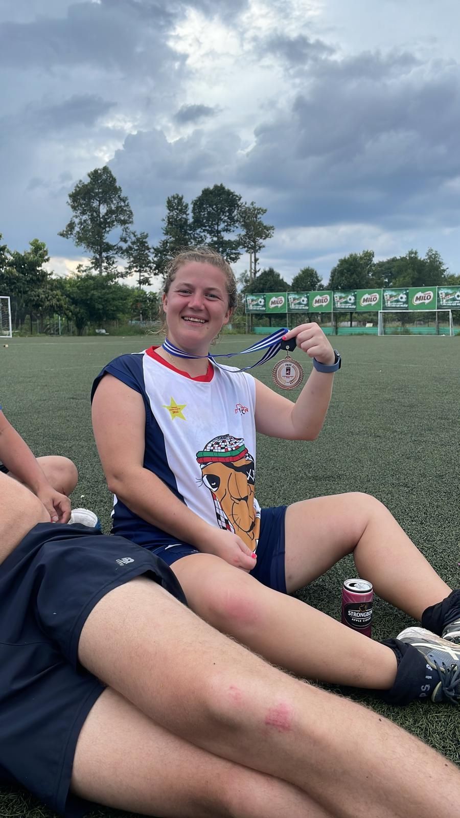 A woman is sitting on the grass holding a medal.