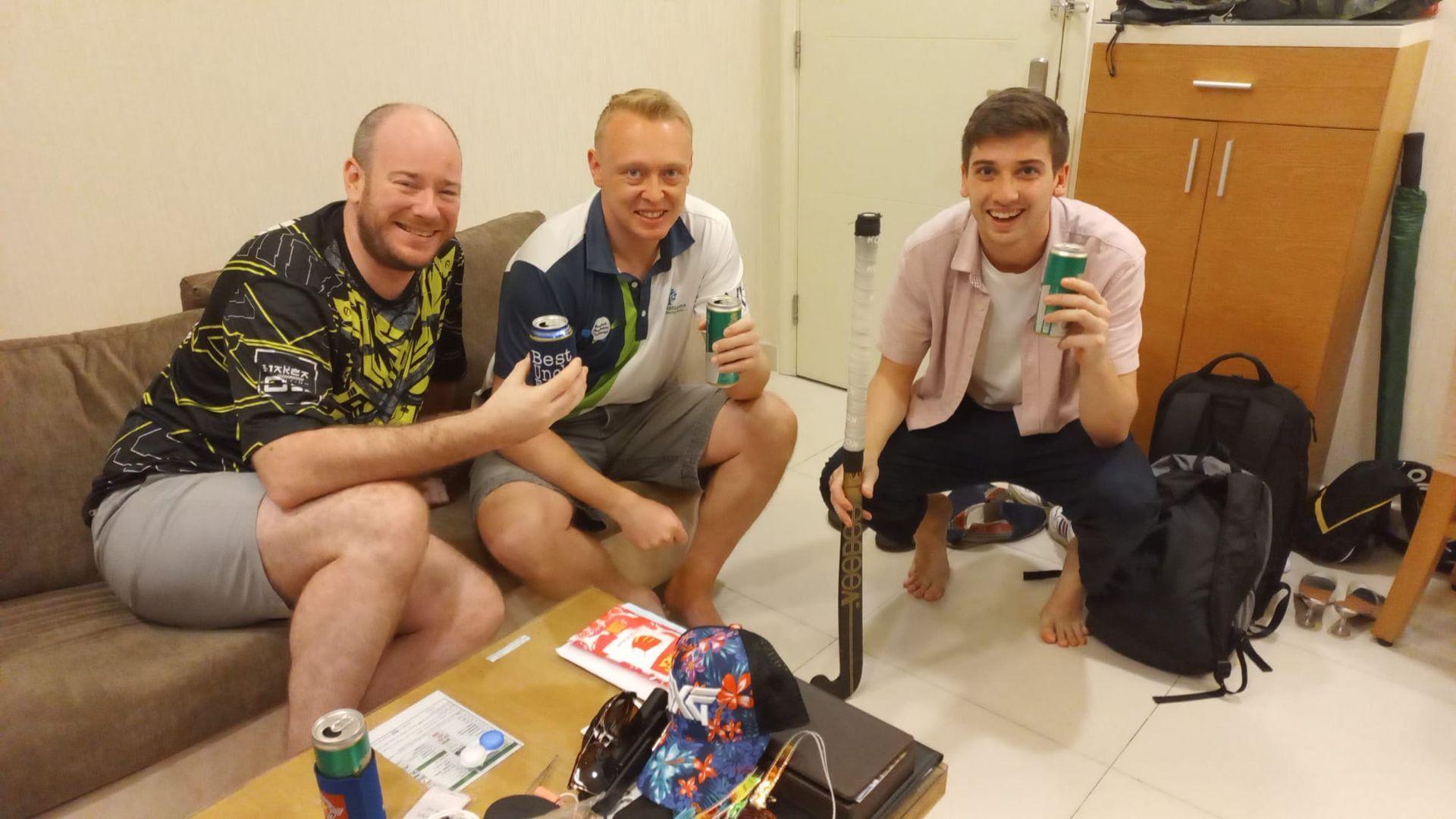 Three men are sitting on a couch holding cans of soda.