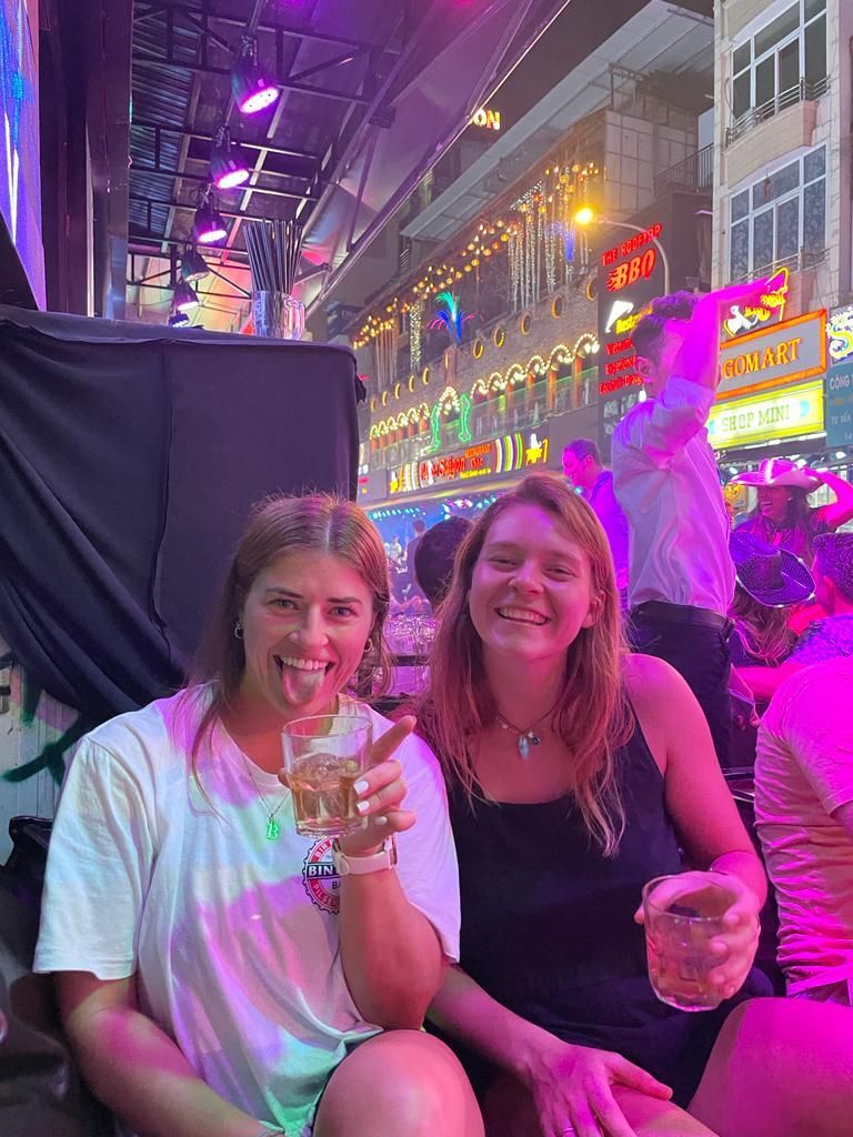Two women are sitting next to each other at a party holding drinks.
