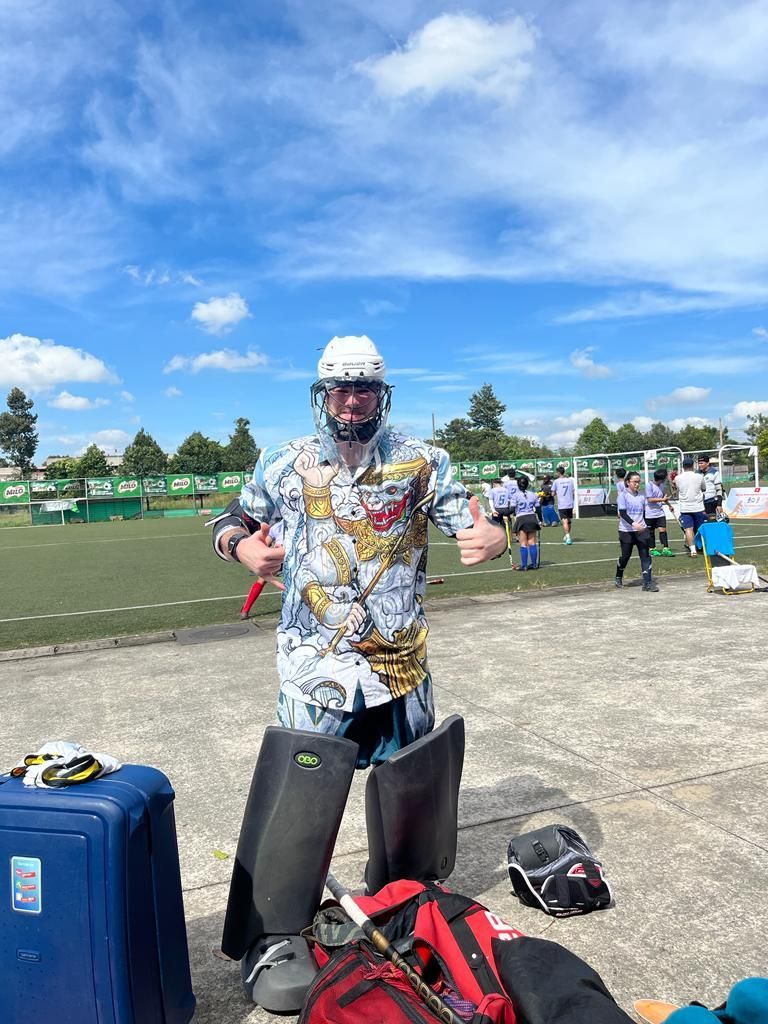 A man wearing a helmet and knee pads is standing in front of a football field.