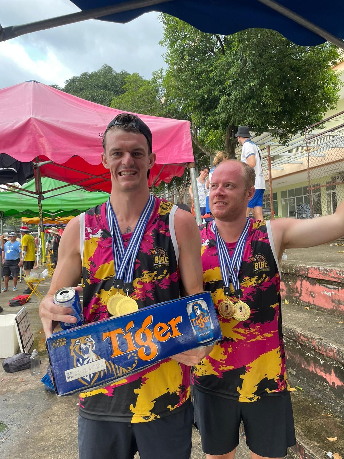 Two men are standing next to each other holding a box of tiger beer.