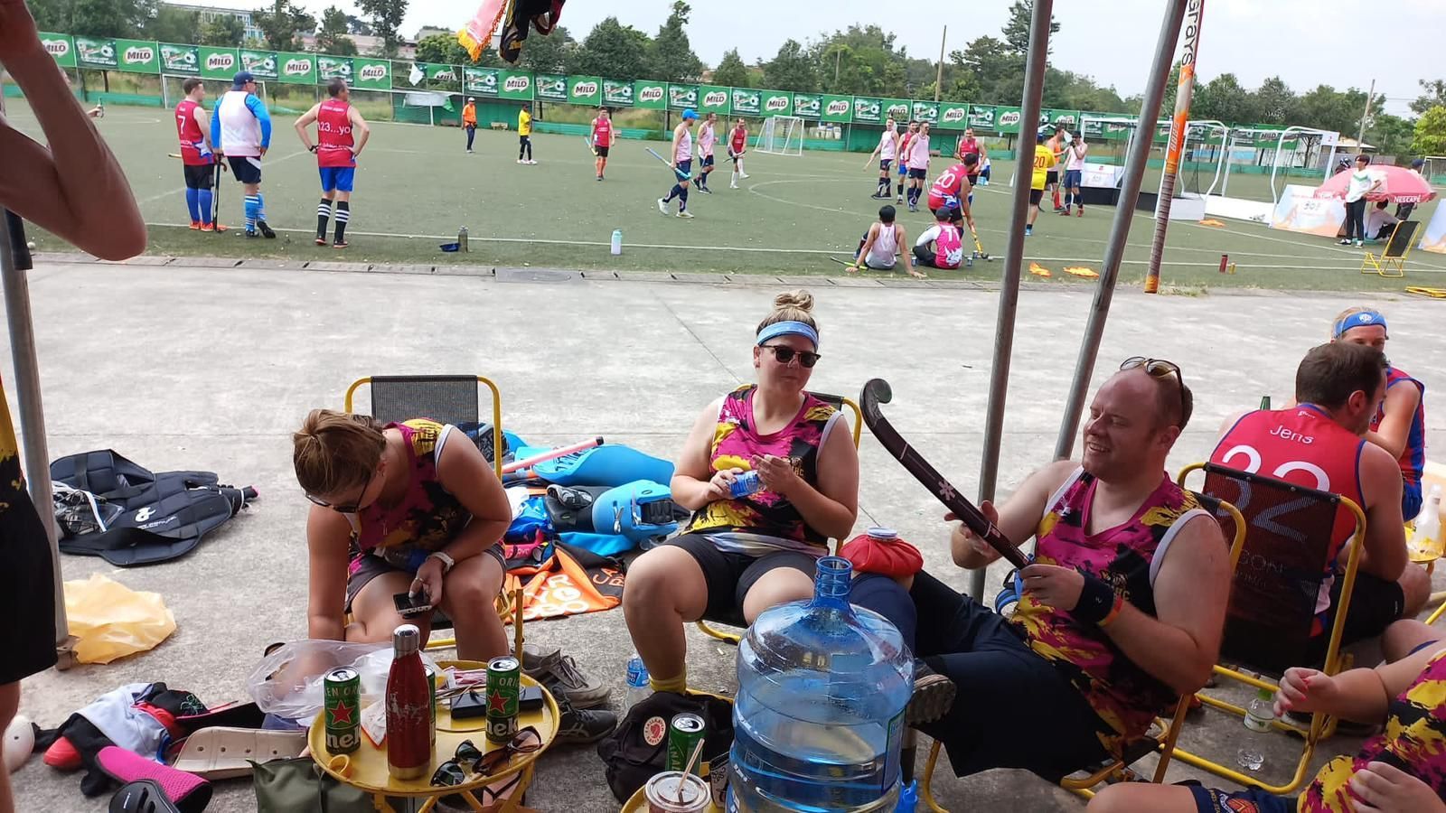 A group of people are sitting under a tent in front of a soccer field.