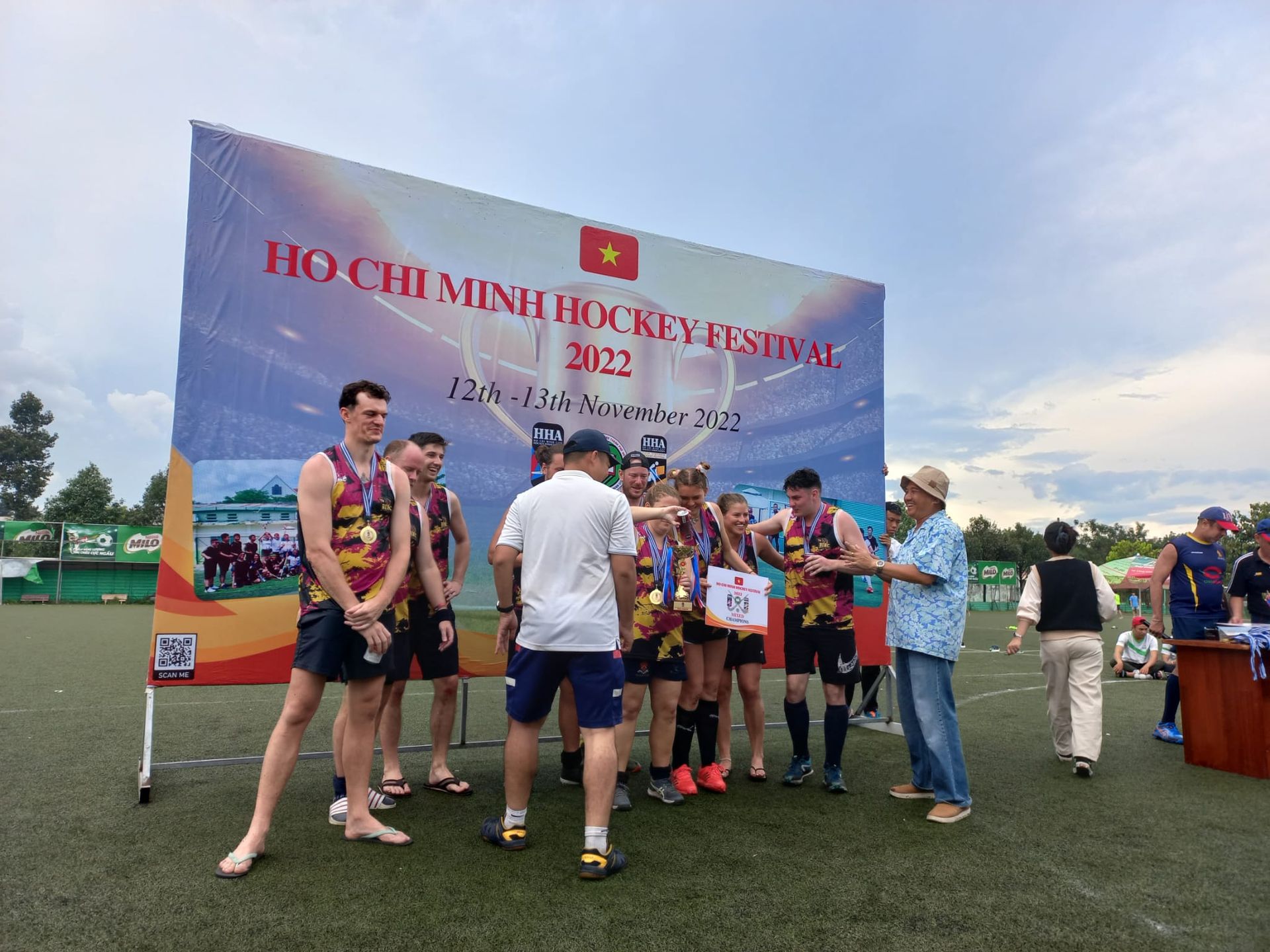 A group of people standing in front of a sign on a field.