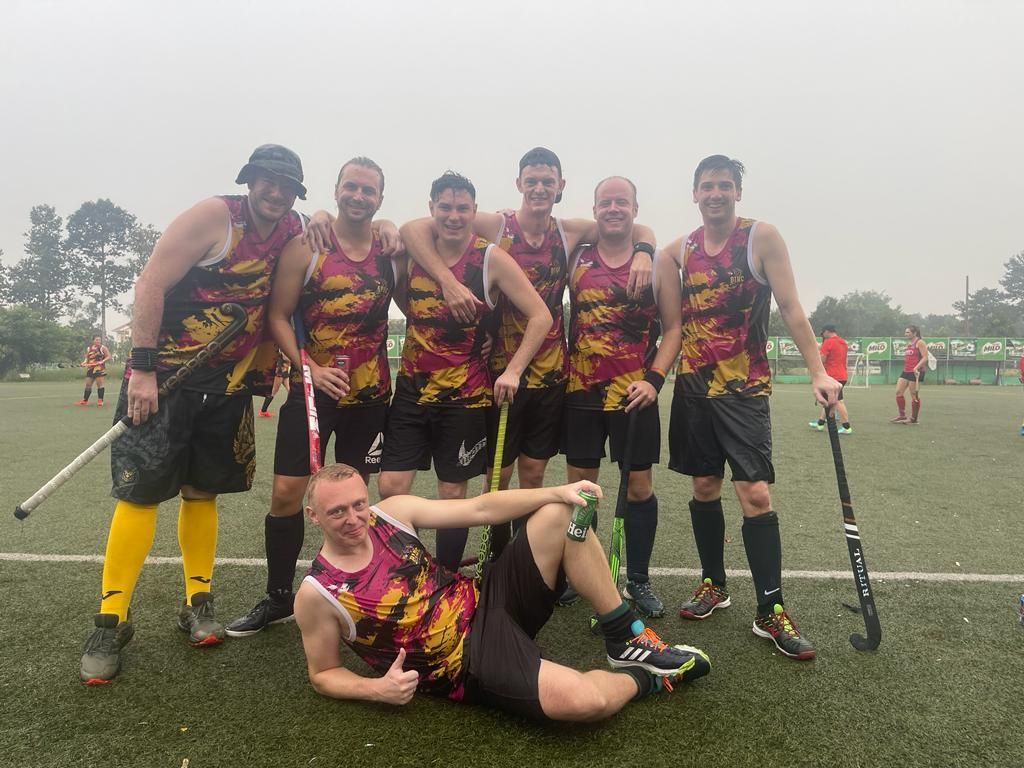 A group of men are posing for a picture on a field while holding hockey sticks.