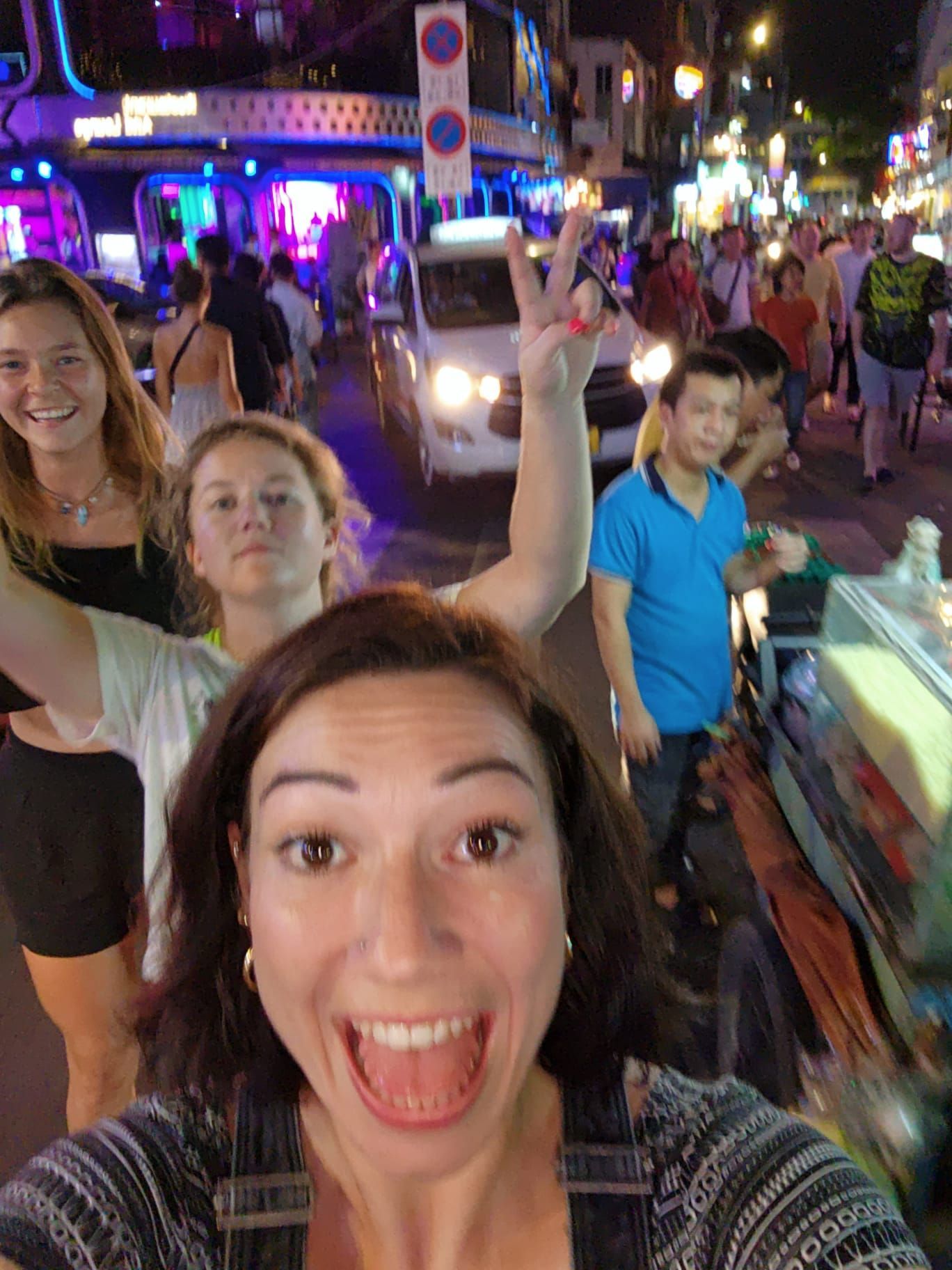 A group of people are taking a selfie on a crowded street at night.