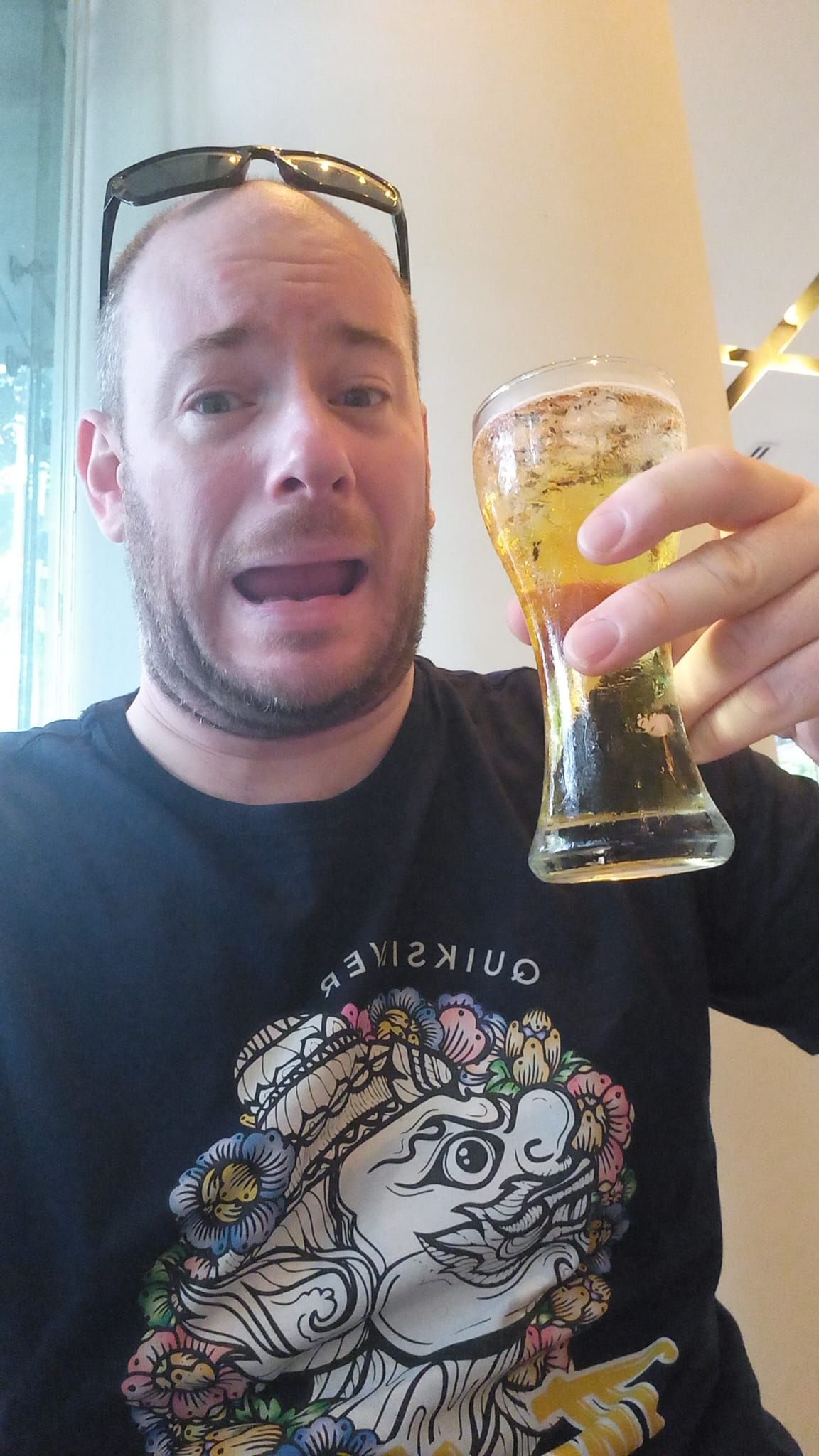 A man in a black shirt is holding a glass of beer.