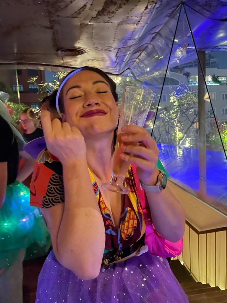 A woman in a purple skirt is holding a glass of wine and making a funny face.