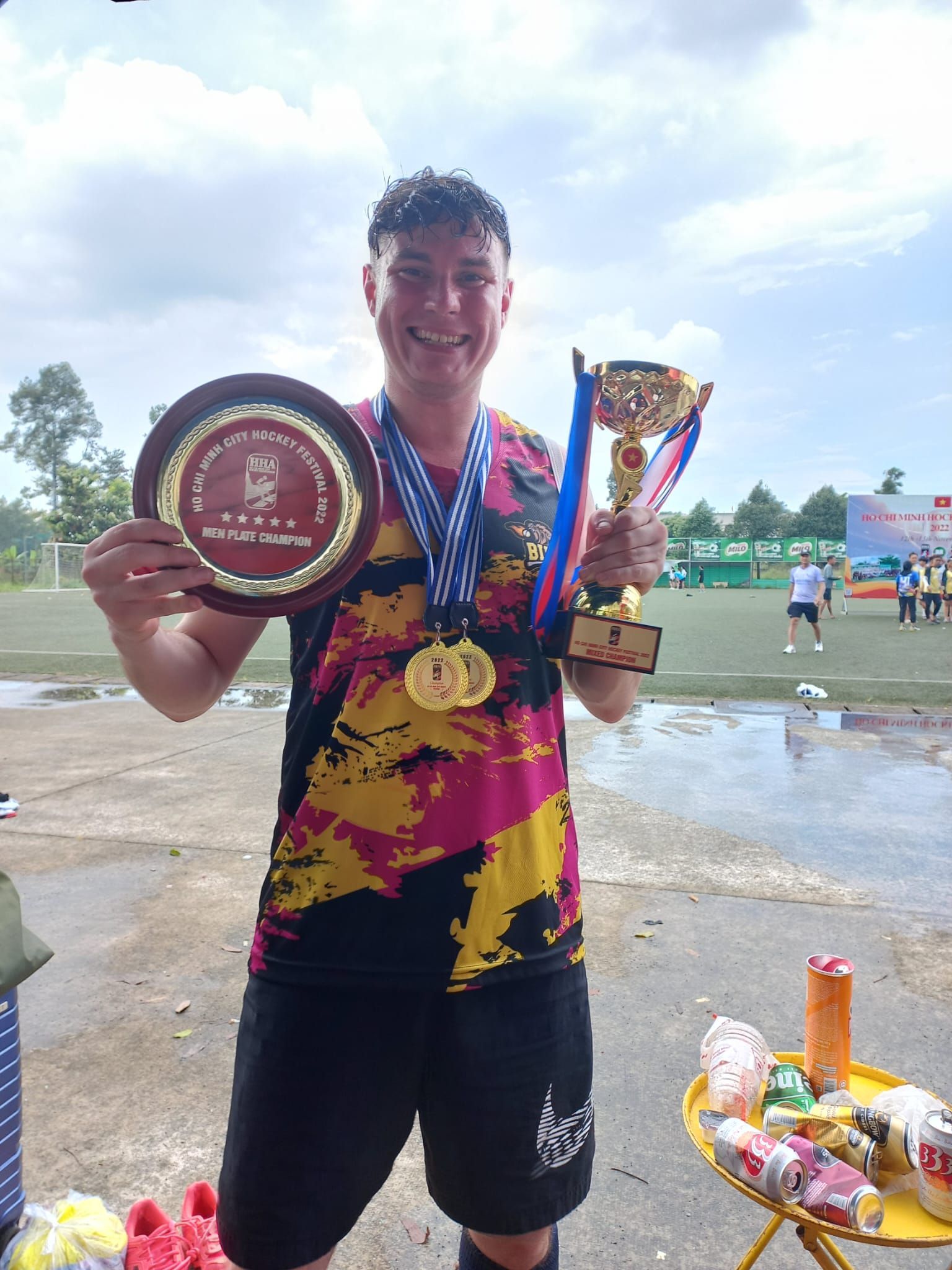 A man is holding two trophies and a medal around his neck.
