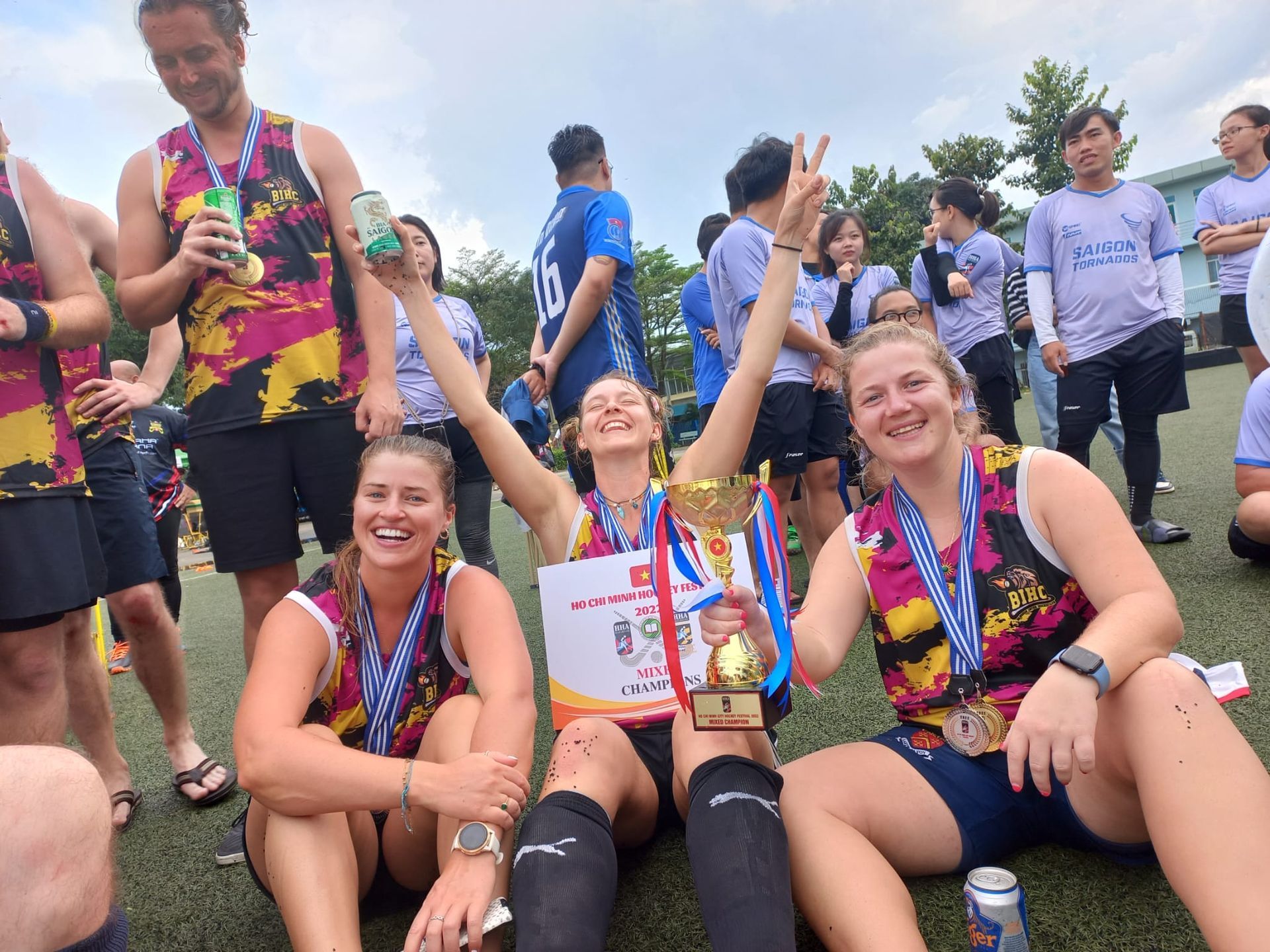 A group of people are sitting on the grass holding trophies and medals.
