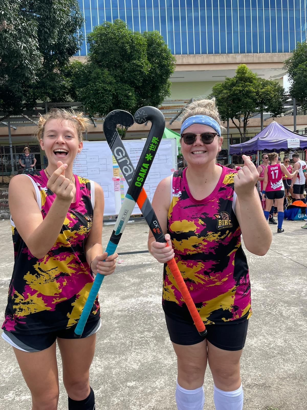 Two women are standing next to each other holding hockey sticks.