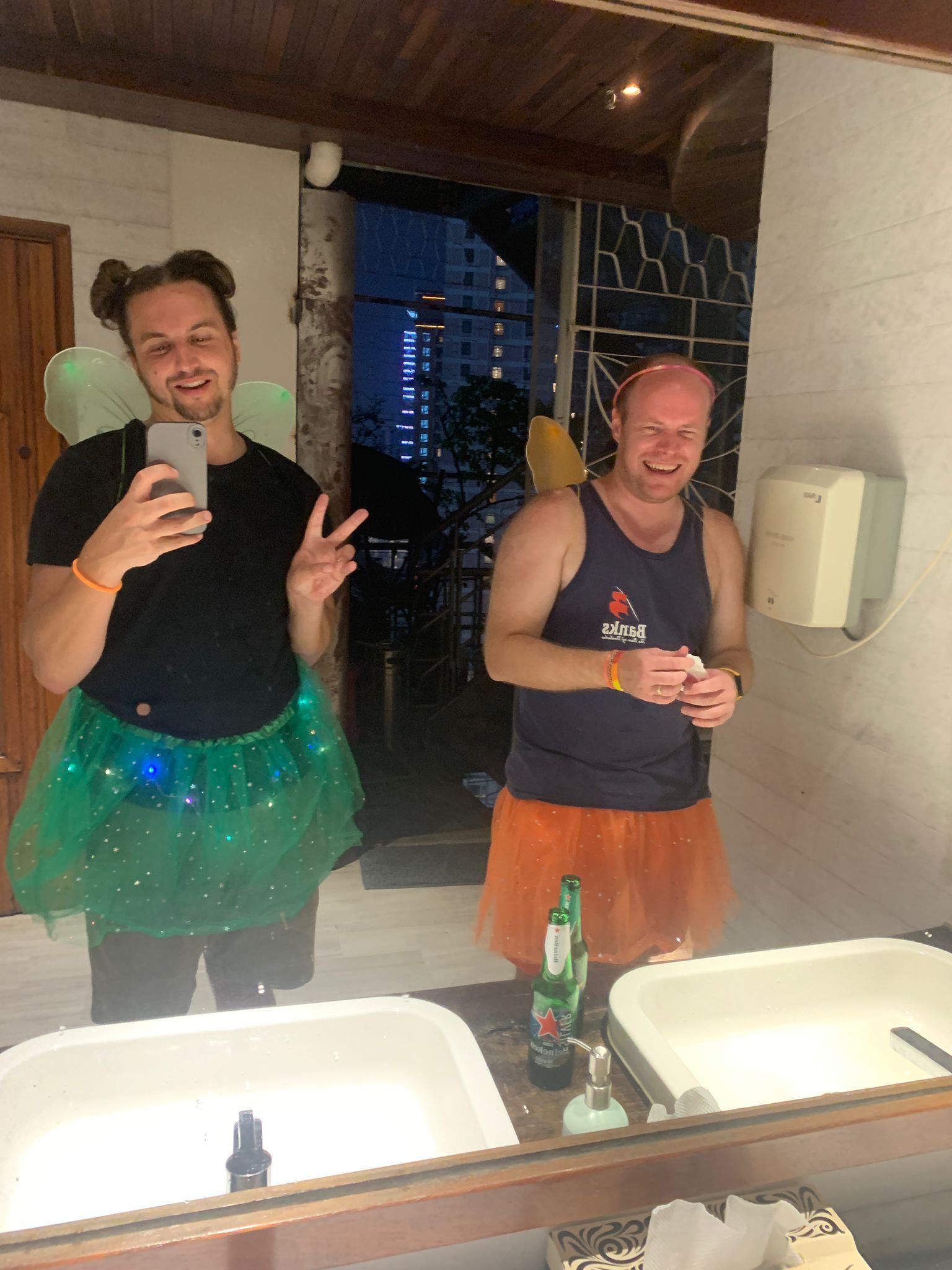 Two men are taking a picture of themselves in a bathroom mirror.
