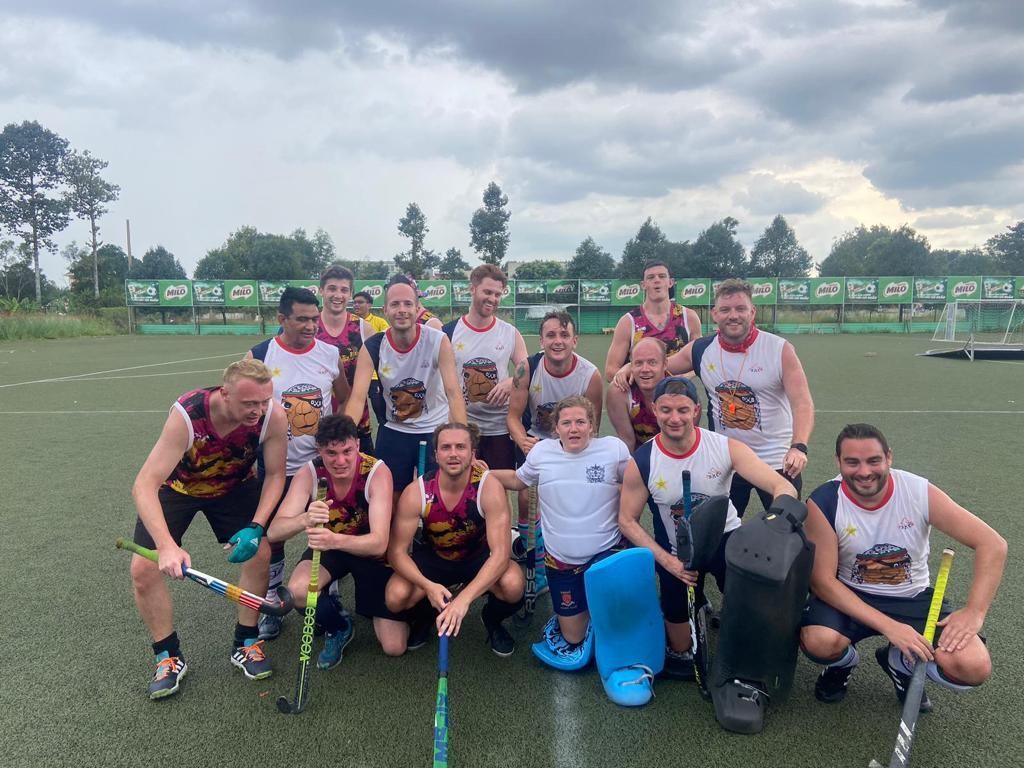 A group of men are posing for a picture on a field with hockey sticks.