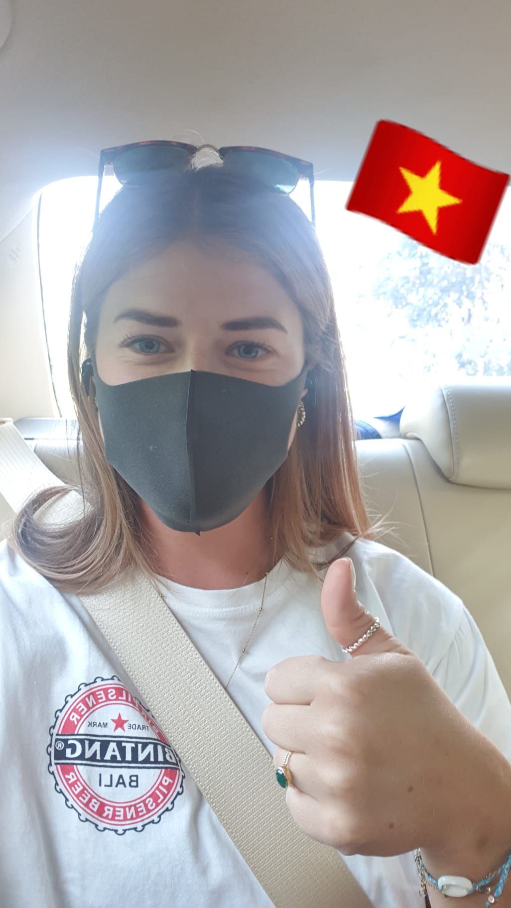 A woman wearing a mask is giving a thumbs up in a car.