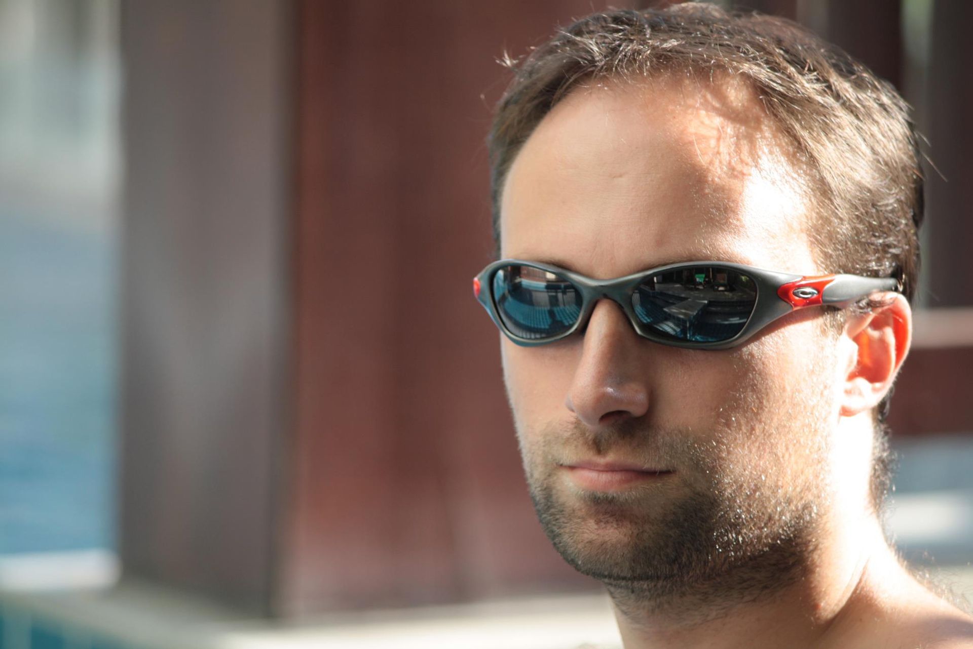 A man wearing sunglasses is standing in front of a pool.
