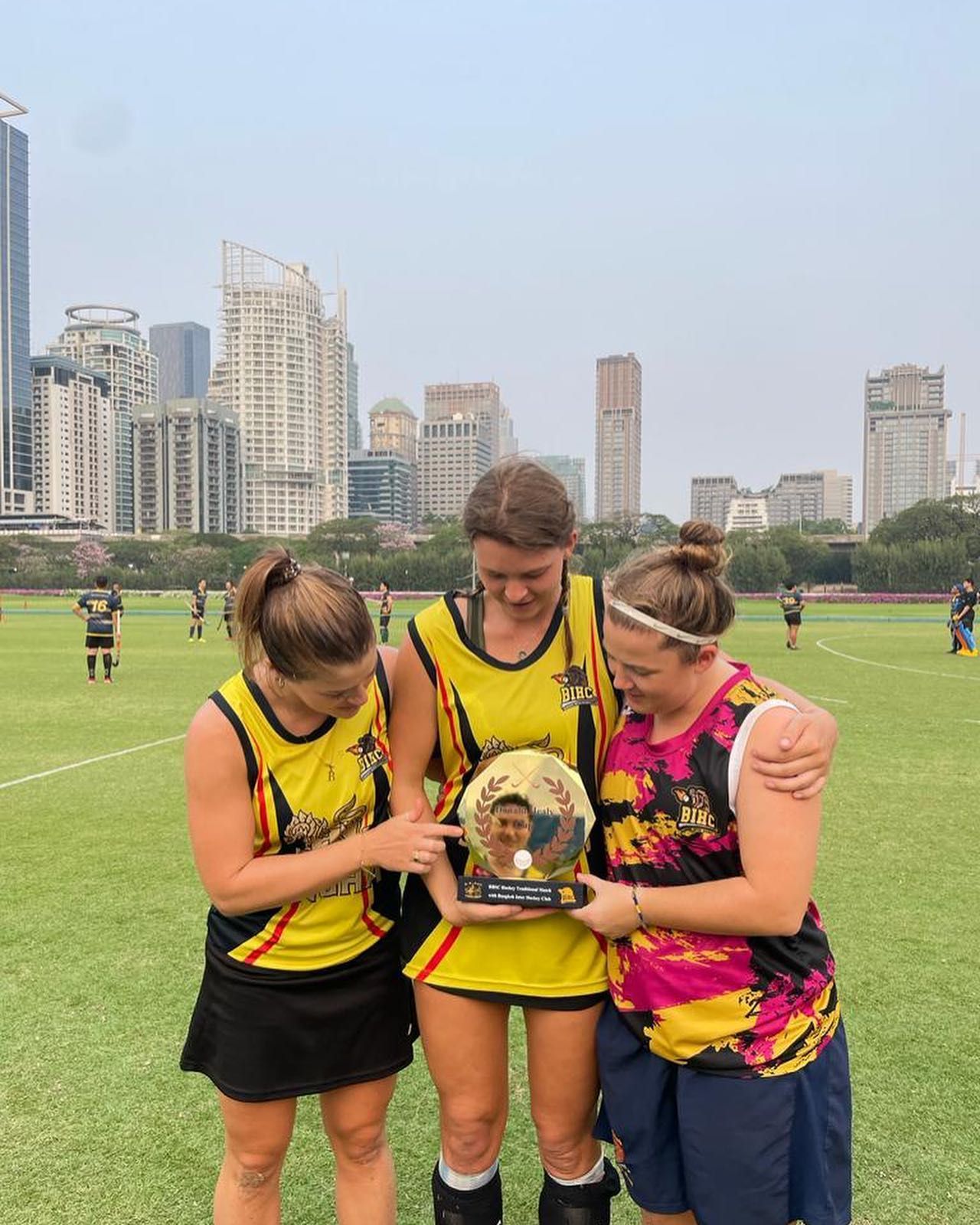Three women are standing on a field holding a trophy.