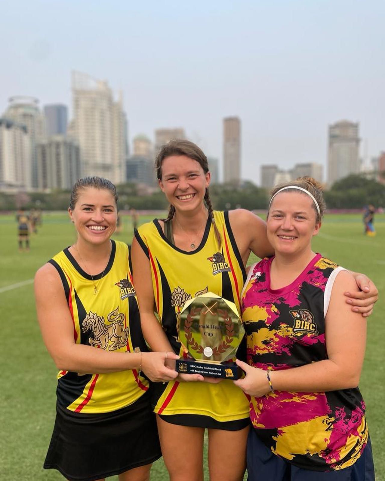 Three women are standing next to each other on a field holding a trophy.