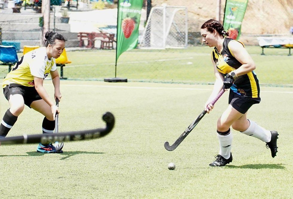 Two women are playing field hockey on a field