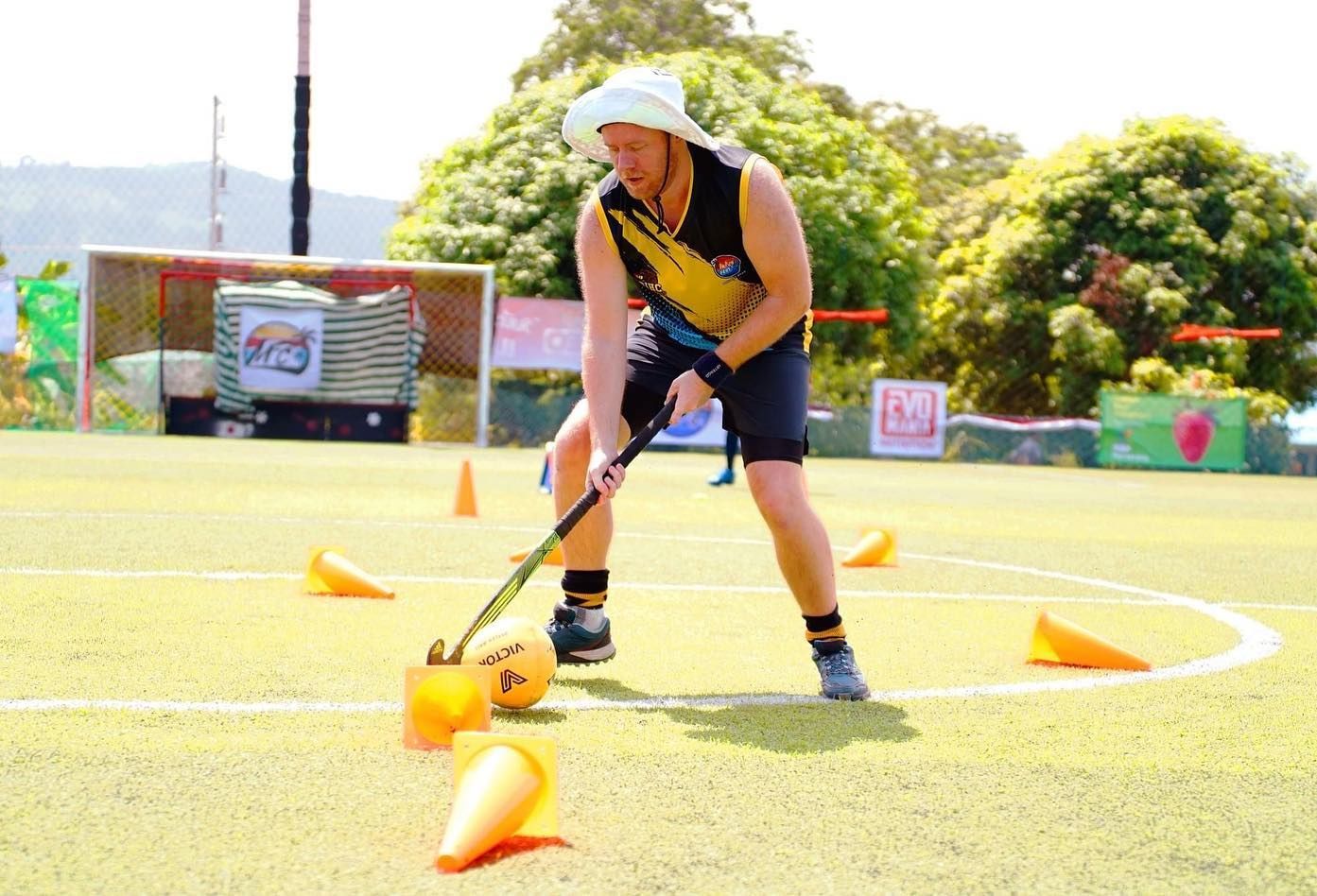 A man is playing field hockey on a field with cones.