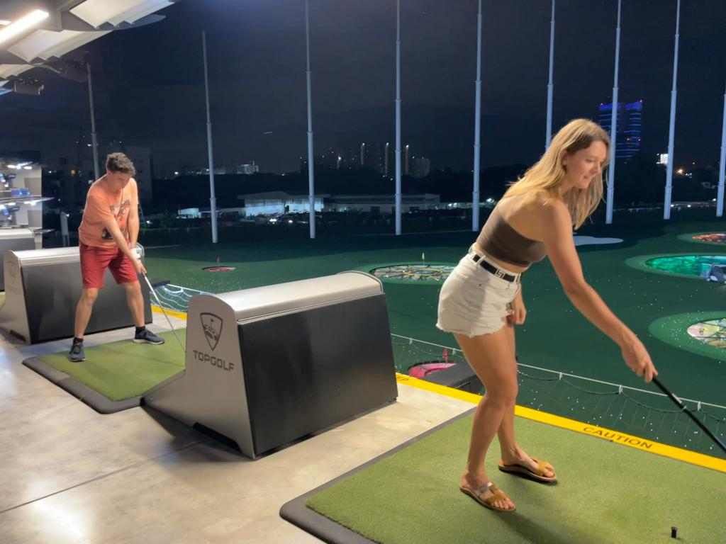 A man and a woman are playing golf on a driving range at night.