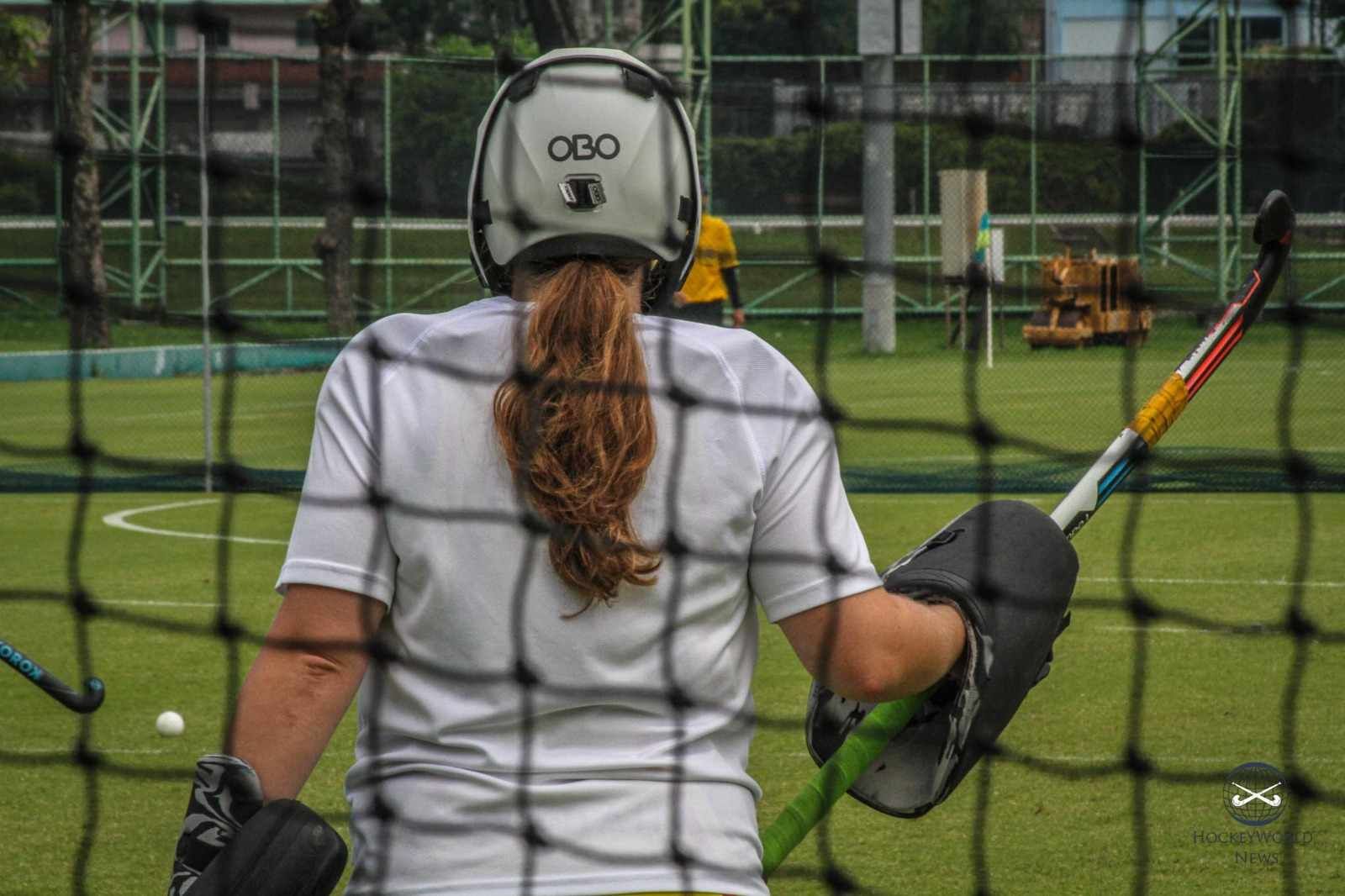 A woman is holding a hockey stick behind a net on a field.
