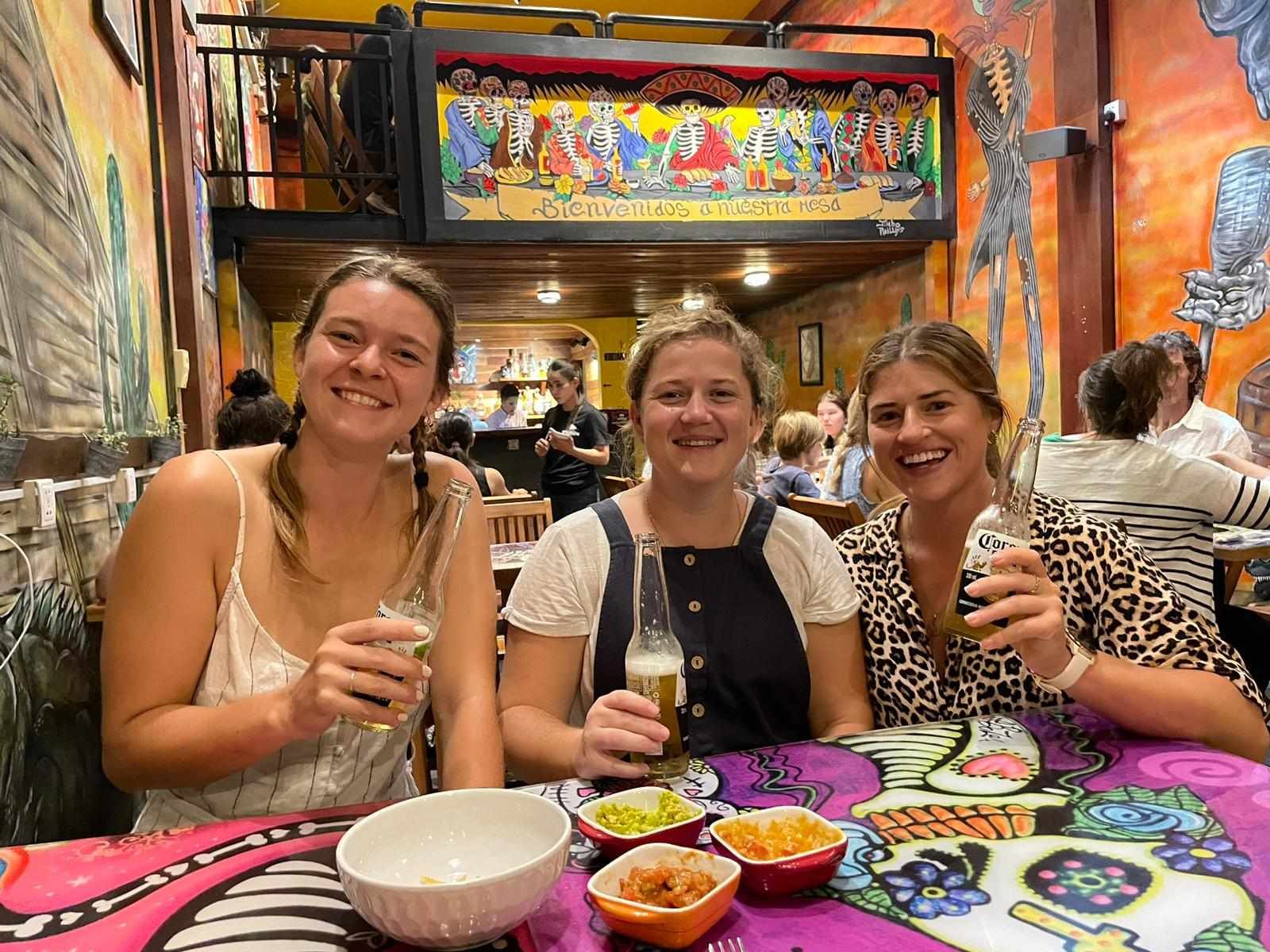 Three women are sitting at a table in a restaurant holding drinks.