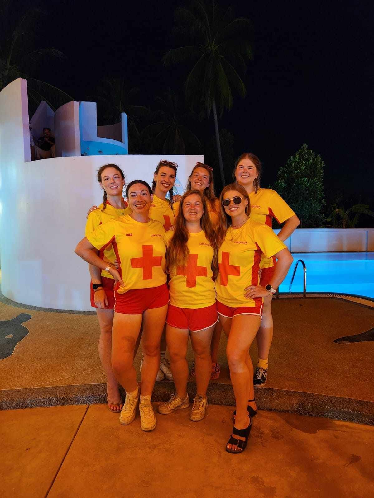 A group of women are posing for a picture in front of a pool at night.