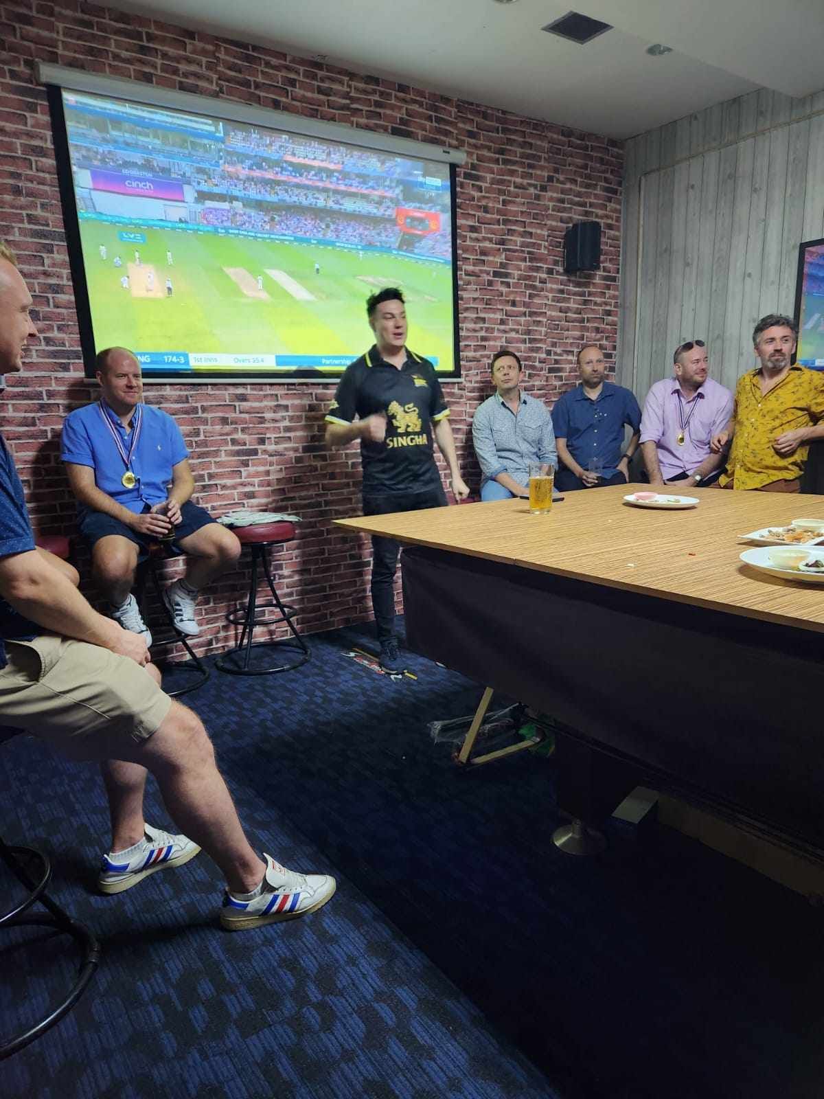 A group of men are sitting around a table in front of a projector screen.