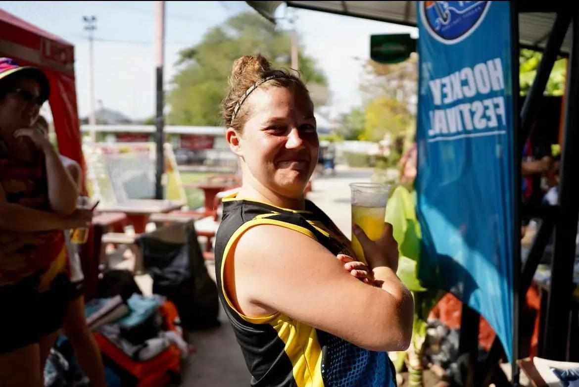 A woman holding a glass of beer in front of a banner that says hockey