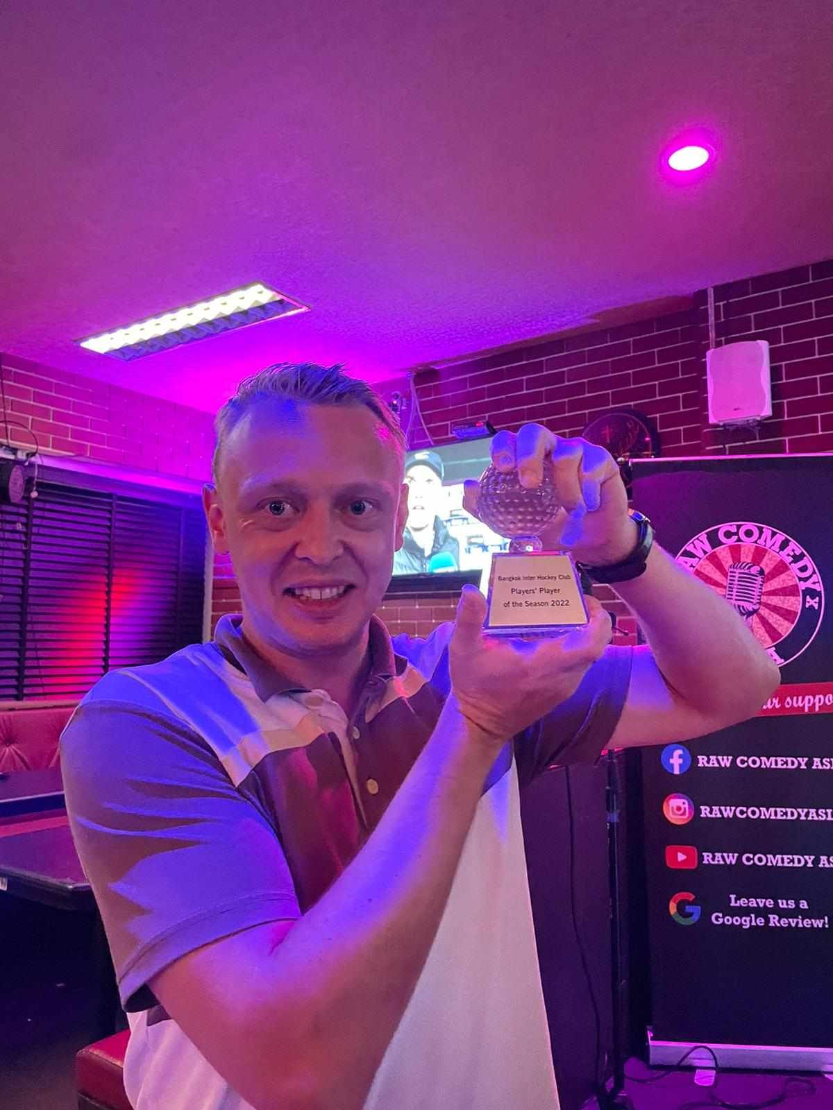 A man is holding a trophy in his hands in a dark room.