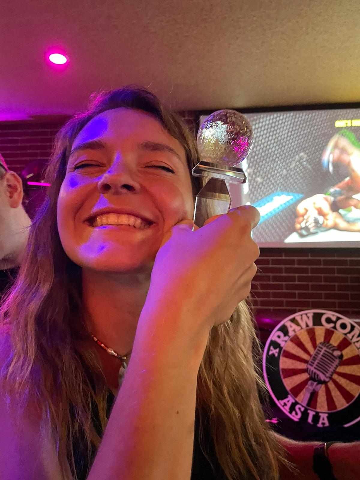 A woman is holding a microphone in front of her face and smiling.