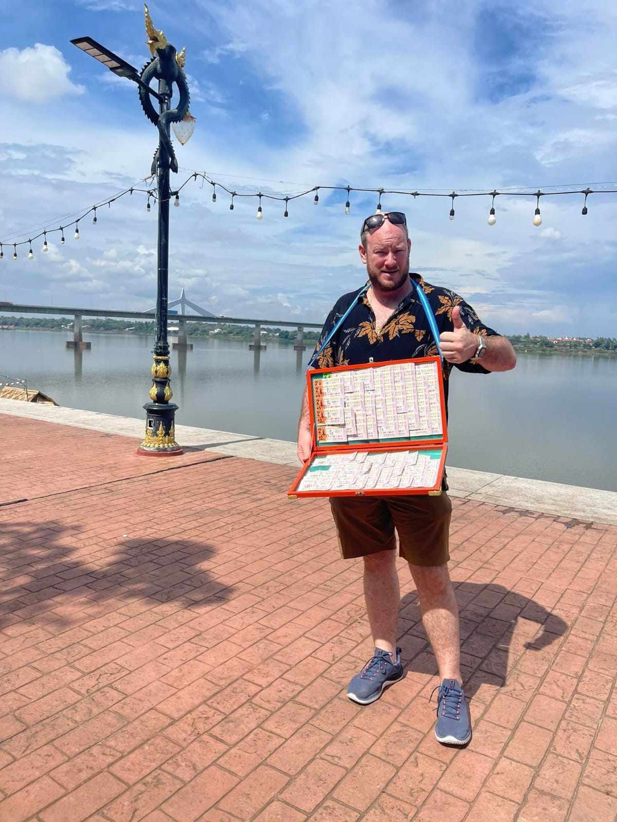 A man is standing on a brick sidewalk holding a box of lottery tickets.