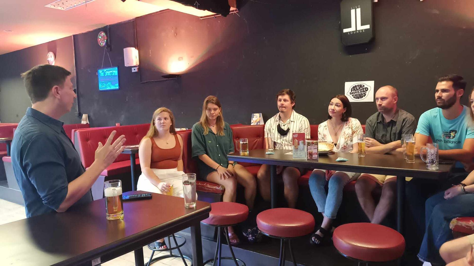 A man is talking to a group of people sitting at tables in a restaurant.
