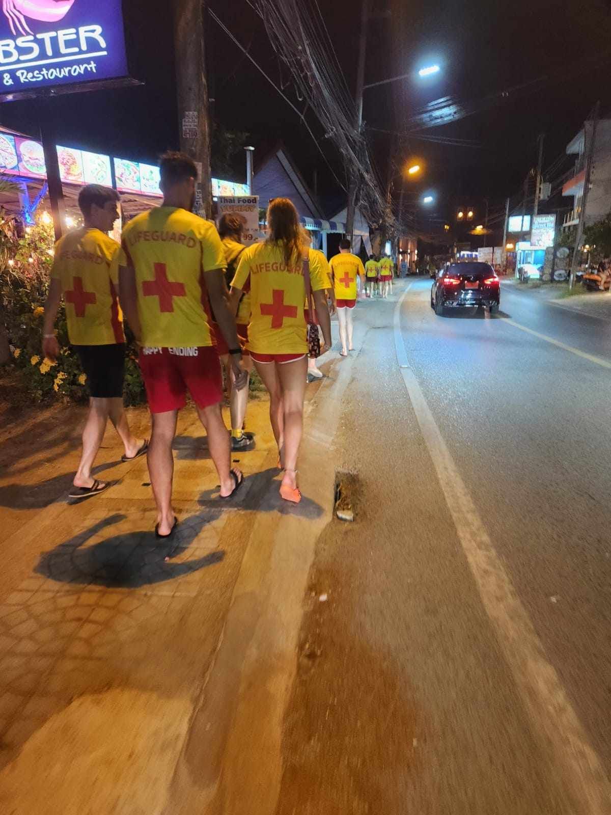A group of people are walking down a street at night.
